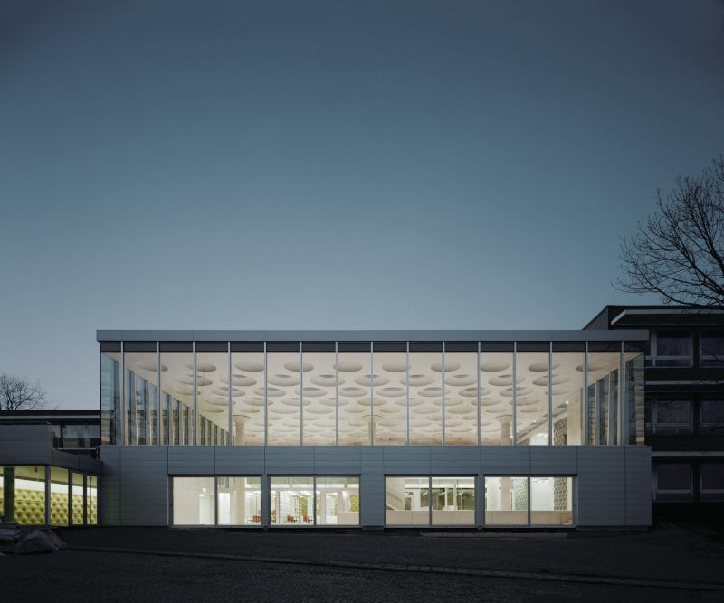 The exterior incorporates an aluminum rainscreen from Kalzip and a curtainwall from Schüco. Ecker describes the existing 11-building, 1960s complex as “well-built, but quiet,” in an aesthetic worth respecting. “We found that we could reinterpret that on the outside,” Ecker says. Visible through the high-efficiency glass from Glas Trösch is the main assembly hall and its three rotationally cast concrete columns that support the mass of the concrete ceiling.