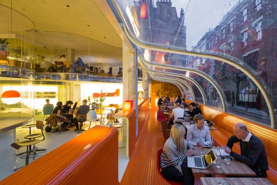 The bright orange color of the storefront caf&eacute; helps identify Second Home to passersby. Mirrored acrylic delineates the floor plate and reflects distorted views of the outdoors.