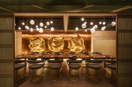 A private dining space offers tables and chairs by Champion Design + Furniture, before a custom art piece of brass-finished wire mesh, which pays homage to the shape of oysters. 