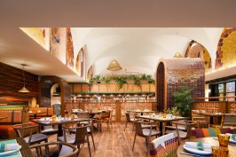Tile archways lead to a raised dining platform with custom, hand-painted wall tiles. Yellow, cream, orange, and purple acoustic panels clad the walls, reminiscent of kernels of heritage corn, serving to incorporate core ingredients of the cuisine seamlessly into the visual language of the space.