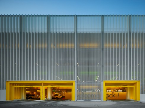 An architectural veil stretches over structural concrete and is punctuated by yellow entry portals.  