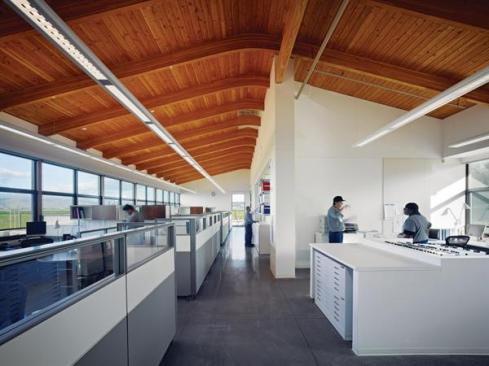 The long, barlike volume of the building is only 38 feet wide, so the interior of the single-story structure is airy and daylit from both sides. This reduces the need for artificial lighting during the day, especially in the relatively densely packed operations area, where there are no walls to inhibit daylight penetration. White walls and neutral finishes highlight the Douglas fir ceiling, which is constructed from tongue-and-groove decking over glulam beams. Often there is so much attention paid to photovoltaics or geothermal as a way of saving energy, Souza says, that low-tech solutions such as these are ignored.