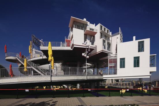 Dutch pavilion - John Körmeling

The Netherlands' kitschy pavilion, called "Happy Street," is an elevated figure eight with more than 20 small houses. One loop of the figure eight encircles a yellow building in the shape of a tulip.