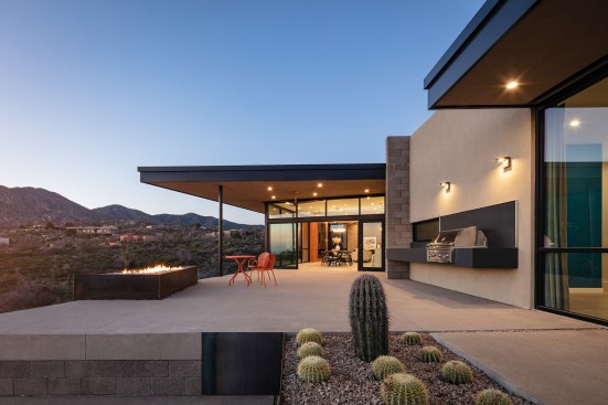 View of main living area patio from the master side patio.  Raw steel fire feature and outdoor, floating BBQ create the lifestyle elements used most by the homeowners.  Angled roof facia helps frame the view of the mountain beyond mountains beyond.