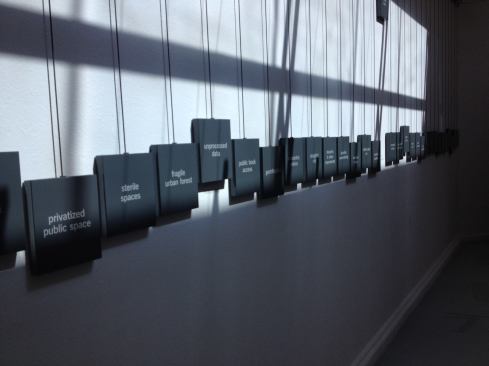 Each banner is hung on a pulley system; when the banner is pulled down, a corresponding counterweight (inscribed with keywords relating to the project) is lifted.