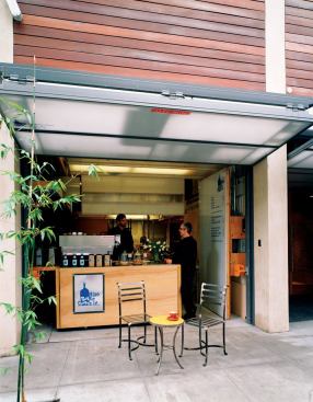 Ground-level garage doors lift up, creating inviting sidewalk space for the Blue Bottle Coffee kiosk. ?