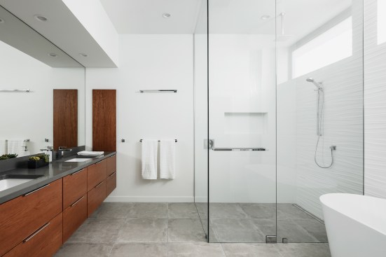 Floating vanity cabinets with dark gray quartz counters span across the main wall of the master bath.  A step free shower with frameless glass and a free-standing tub are balanced by a 3d tile wall.
