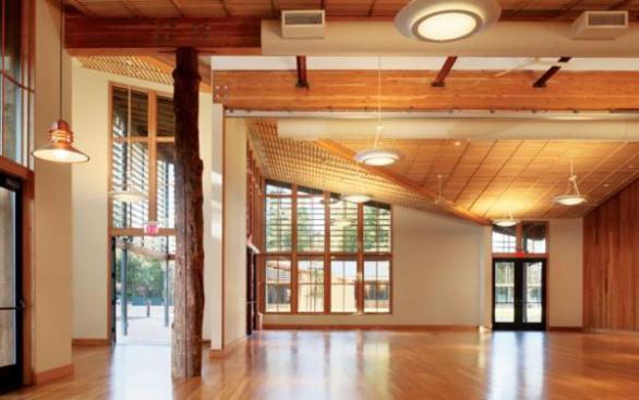 The community room in the town center's community hall is a multipurpose space designed to allow for meetings, parties, and other events. Supporting the roof is a tree column?an unusual construction that wraps a steel-pipe support with the split trunk of one of the trees felled to make way for the complex's sports fields. Multiple doors and windows can be opened to make the room an indoor/outdoor space during the milder months.