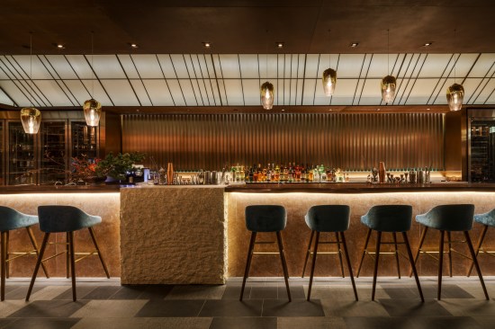 A solid walnut top and pink marble front form the bar; behind it, panels of copper and oxidized steel rotate to create a rippling effect. 