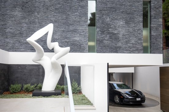 Modern luxury home entry with Richard Erdman sculpture and textured stacked stone walls.