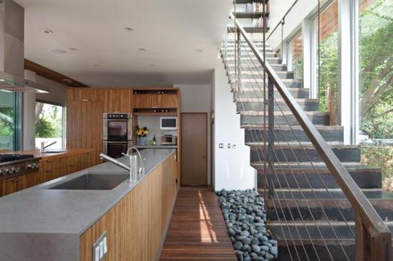 Two long counters serve as the rooms work surfaces. The steel stair casts a shadow of smooth stones.