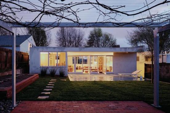In the backyard, an existing 70-year-old grapevine grows over a new galvanized steel trellis, inspired by the sleeping porches of Schindlers Kings Road house.