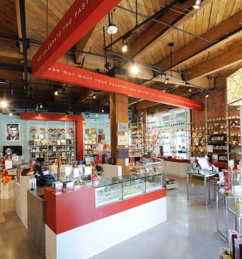Sixth Floor Museum Store + Caf&eacute;- Dallas, TX The SFM Store + Cafe is a small adaptive use project overlooking Dealey Plaza. The project provides an immersive retail environment for the museum's gift shop, including a 34-seat casual caf&eacute;. The design aims to work with the existing building--a turn of the century warehouse building-- in a'ship-in-a-bottle' strategy that touches the shell lightly with a clean lined and modern design that clearly differentiates new from existing. A new exterior sign carefully woven in the historic fa&ccedil;ade hints at the new interior. The angles present in the arrangement of program elements respond to the desire lines and views to the components of the museum's campus: the site of the event and the entry to the museum. Scarlet fragments of these visual frames appear as a motif that ties the diverse functions into a cohesive whole. The colorful design elements effectively establish a fresh look for the museum's branded image. 
Architect: Corgan Associates