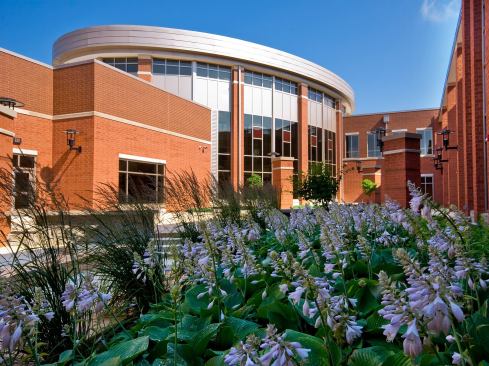 Plainfield High School-Plainfield, Indiana The new Plainfield High School was developed to be a community campus--to provide warmth, character, and a sense of place. A ribbon concept connects the building to the exterior site through a major pedestrian pathway that weaves out of the building's athletic event entry to the exterior athletic complex, providing accessibility to all fields and support buildings. An internal "street" creates a clear circulation path within the 494,000-square-foot facility and links the three major building pavilions--fine arts, academics, and student athletic programs. The building's horizontal massing, roof forms, and palette of brick--with stone trim and vertical glazed openings with colored accent glazing--draw their inspiration from elements of the Prairie Style. 
Architect: Schmidt Associates