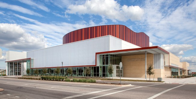 The wood finish of the auditorium's perimeter walls appears to extend up through the center's roof, where the auditorium is clad in metal panels, in a variety of hues and widths to mimic the character of wood.