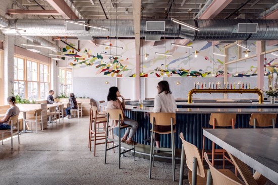 The restaurant and bar is split into different zones of seating to accommodate different groups and activities; sound is baffled by felt under the tables and in panels on the walls, which feature murals by local artist Madison van Rijn. Muuto chairs and light fixtures by Lambert & Fils accent the space. 