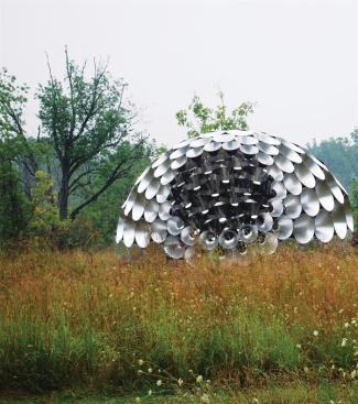 The reflectivity of the aluminum cones picks up the colors of the pavilion's environment. But the geometry of the cones themselves creates an interesting visual trick. The lower curve of each piece reflects the sky, and the upper curve reflects the ground plane, creating an inverse relationship with the surrounding landscape.