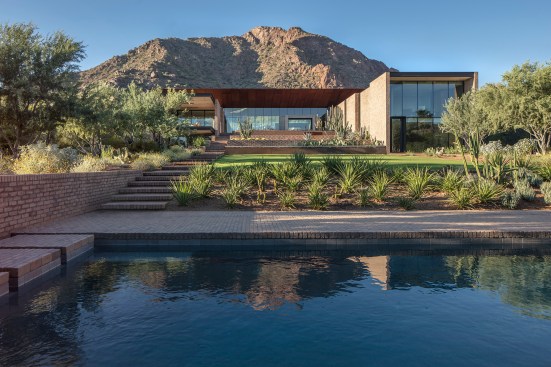 The terracing of the site, which is filled with native plantings, is evident in this view from the pool house. The wings for the bedroom and services, as well as the expansive roof on the main house, sheathed in pre-weathered Cor-Ten steel panels by Metal Man, provide shade.