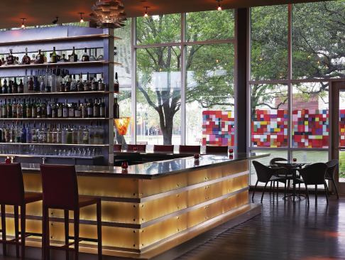 The bar at The Grove is clad in glowing panels that mimic a rich material like alabaster. The effect is achieved by using 3form resin panels back-lit by fiber-optic strands that give the panels a gentle glow. Those perched on a bar stool enjoying one of the restaurant’s signature drinks also have a frontrow view of artist Margo Sawyer’s wall of color blocks, a feature that fits well with Discovery Green’s commitment to public art.