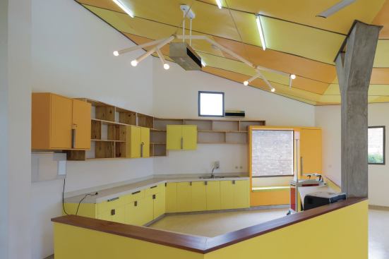Inside the infusion room, which is the center’s largest space, custom millwork and a nurse’s station are all painted in vivid yellow shades from Ameki Color. A custom light fixture hangs from the steel frame and painted plywood ceiling.