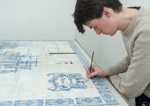 A ceramics conservator working on a framed set of 113 Delftware tiles showing a whaling scene. 