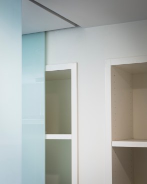 Removing headers from around the bathroom space helped visually heighten the space, but removed the traditional means for hanging doors. Instead, the team installed sliding glass panels that move through channels in the ceiling.
