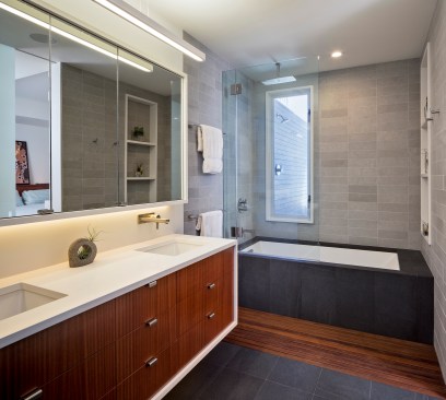 Transom windows and glass panels allow plenty of light to penetrate the bathroom, shedding welcome natural light on dark, earthy materials.