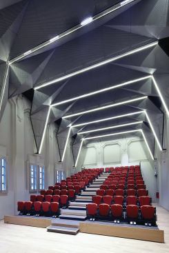 Pleated mesh screens by SCDA Architects clad the ceiling of the auditorium, which was formerly a chapel.