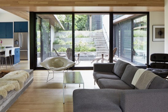 Living room interior, with view of terraced, landscaped courtyard and studio–garage pavilion