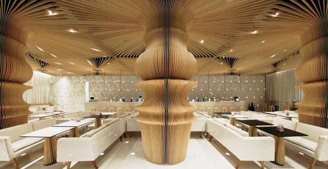 The space is anchored by a series of columns clad in plywood slats that are CNC-routed to emulate a lathe-turned table leg. 