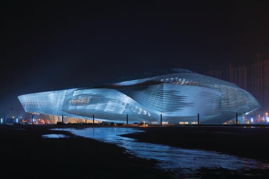 At night, dramatic lighting plays off of the parametrically designed aluminum skin of the Dalian International Conference Center.