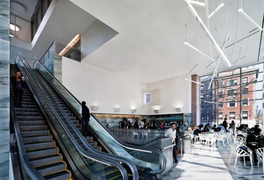 A stair leads to a second-floor café that anchors a four-story glazed atrium with escalators to the library and research elevator core above.