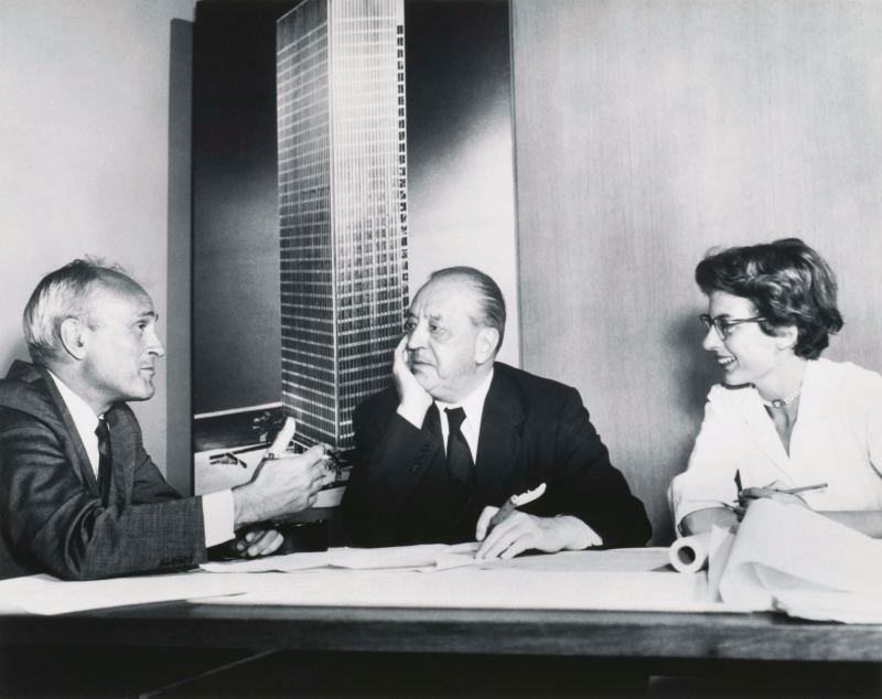 Philip Johnson, Ludwig Mies van Der Rohe, and Phyllis Lambert discuss the Seagram in front of an image of the building model soon after she helped the architects win the commission in 1955.