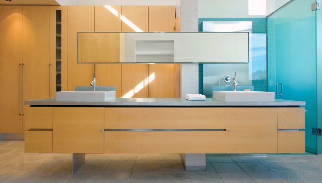 Wide drawers with recessed aluminum handles hold quotidian bathroom supplies; glass shelves behind a stainless steel shower screen house shampoo and soap.