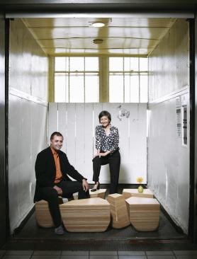 Jeffrey L. Day and E.B. Min pose on the Stones Table, which melds organic form with CNC precision. Together, the pieces form a rectangular table.