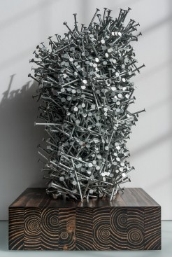 “Unfastened” aggregates approximately 3,900 nails on a 2-foot-by-4-foot stained wood base.